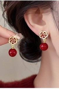 Détail de boucles d'oreilles rose rouge dorées avec zircon et pendentif perle brillante