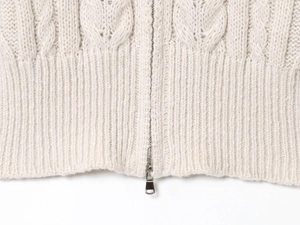 Detail of chunky cable knit texture and silver metal zipper on a beige cardigan sweater