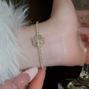 Close-up of golden four-leaf clover bracelet with sparkling zircon stones and tennis chain