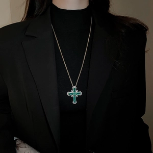 Gros plan du pendentif croix en cristal vert avec chaîne dorée sur un pull noir