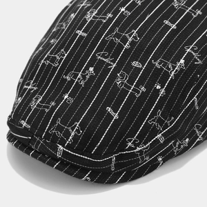 Gros plan du béret noir à motif de teckel montrant le tissu rayé et les broderies