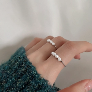 Close-up of four white pearls on a slim silver ring worn on a finger with a soft backdrop