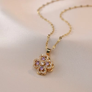 Elegant golden clover necklace featuring white and purple zircons on soft fabric