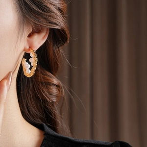 Macro view of C-shaped gold-plated hoop earrings with textured finish and pearls