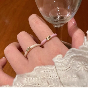 Detail showing two gold rings with cream and pink enamel and rectangular zircons