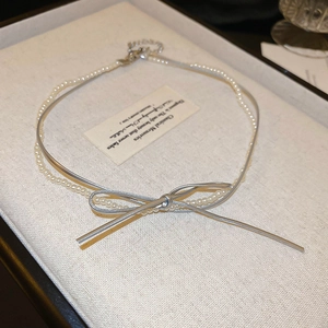 Detail view of double-layered faux leather bow necklace with pearls on a jewelry tray