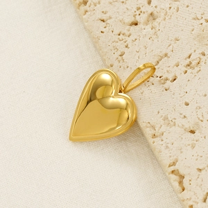 Polished gold heart pendant on beige stone and fabric background, minimalist style