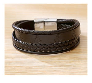 Detail of dark brown braided leather bracelet with anchor pattern and silver metal buckle