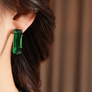Close-up of green rectangular crystal earrings featuring a silver needle and metal claw setting