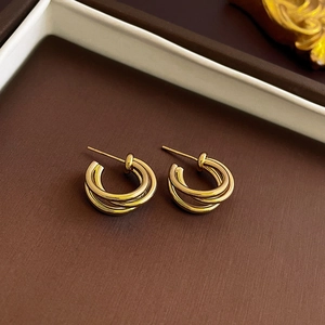 Macro shot of gold-plated triple-layered hoop earrings on a textured brown surface