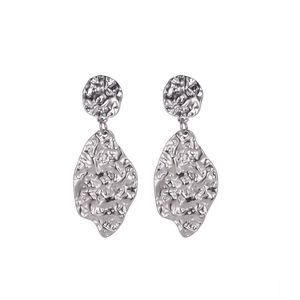 Macro shot of silver titanium steel earrings with irregular hammered texture on white background