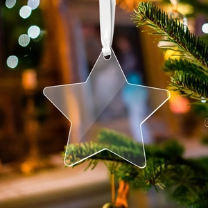 Clear acrylic star ornament with white ribbon hanging on a Christmas tree branch