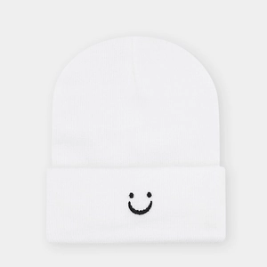 Close-up of white knitted beanie featuring detailed black smiley face embroidery