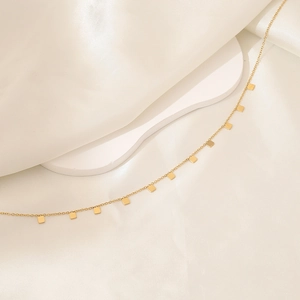 Detailed shot of golden cube charms on a minimalist stainless steel necklace