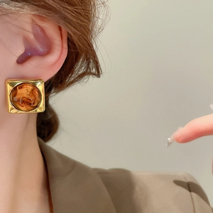 Macro detail of amber resin earrings with a gold frame worn by a side-profile model