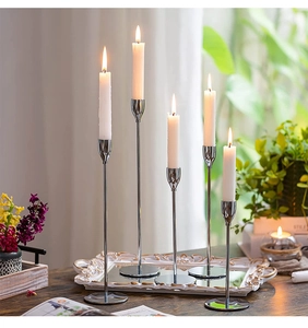 Five silver metal candlesticks with lit white candles on a mirrored decorative tray