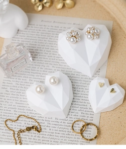 Macro detail of white heart jewelry display stand with elegant pearl earrings and gold ring