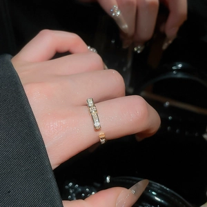 Close-up of golden open ring featuring a sparkling rectangular zircon bar on a model's hand
