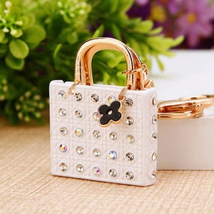 Detail of white mini bag keychain with crystals and a gold chain against flowers