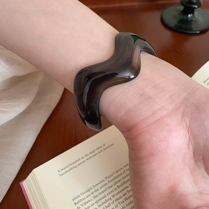 Detail of a wavy dark brown acrylic bracelet with tortoise texture worn on the wrist