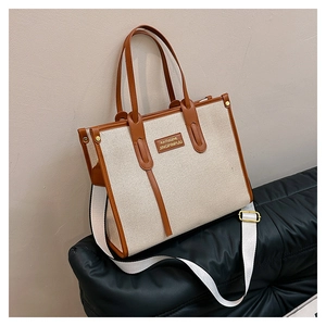 Detail of beige canvas tote with brown leather trim and adjustable shoulder strap
