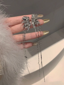 Close-up of sparkling silver star moon tassel earrings worn with elegant white fur outfit