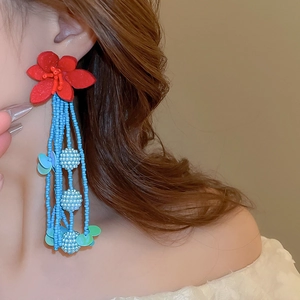Close-up of long tassel earrings with red floral studs and blue beaded strands
