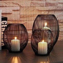 Three black wire candle holders in different sizes on a wooden table with soft lighting