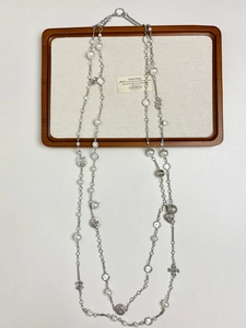 Flat lay of a long silver pearl necklace with diverse heart and clover charms on a tray