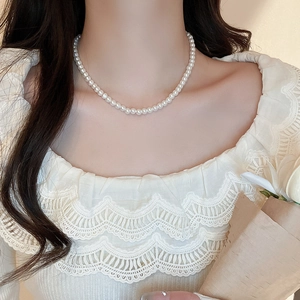 Close-up of minimalist white pearl necklace worn by a model with a lace top