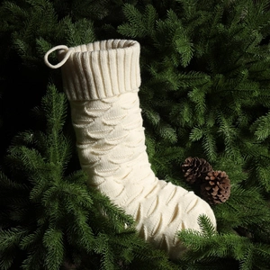 Close-up of cream knit Christmas stocking with thick fish scale texture on pine branch