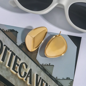 Gepolijste 18K gouden roestvrijstalen kiezel oorknopjes op een modetijdschrift achtergrond