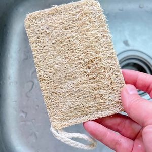 Natural loofah dish sponge with cotton hanging loop held over a kitchen sink