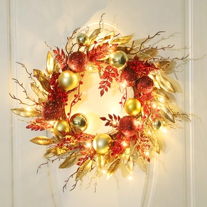 Christmas wreath with red and gold ornaments and warm LED lights on a white wall