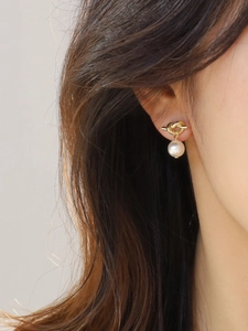 Close-up of a gold knot stud earring with a hanging white pearl on a model