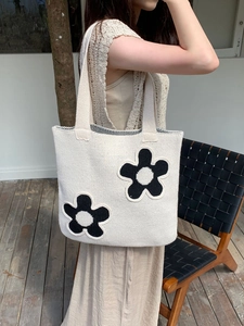 Close-up of cream knitted tote bag with black floral patterns in a natural outdoor setting