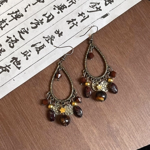 Detail of vintage teardrop earrings with bronze metal and flower charms on wood