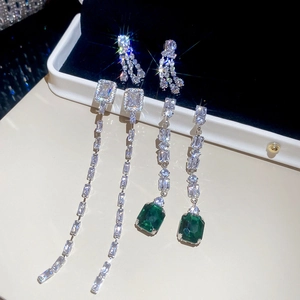 Close-up of sparkling square zircon tassel earrings with emerald and clear stones in a gift box