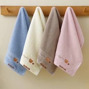 Detail of four soft cotton towels with cartoon bear embroidery hanging on wooden hooks