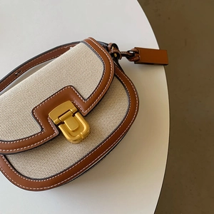 Dettaglio della borsa a sella in tela e pelle con cuciture a contrasto e fibbia dorata