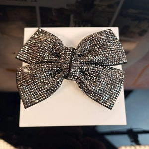 Close-up of a large black bow hair clip with sparkling rhinestones on a white box