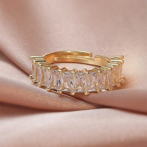 Detailed close-up of golden adjustable ring with baguette-cut zircon on pink silk