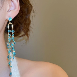 Close-up of long gold fringe earrings with blue crystals worn by a model in soft light
