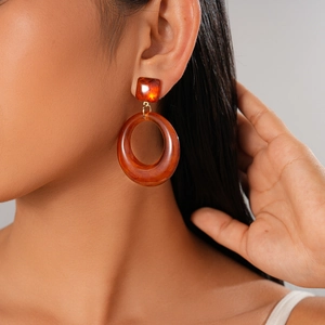 Gros plan sur une boucle d'oreille créole en résine ambre portée par un mannequin