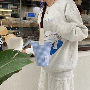Blue gingham canvas bucket pencil case with leather handle shown in a bakery setting