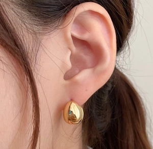 Detailed close-up of golden teardrop earring with smooth mirror finish on model