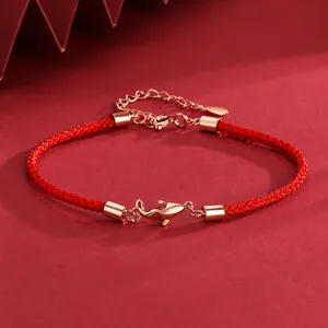 Close-up of woven red cord bracelet featuring a rose gold koi fish charm and clasp