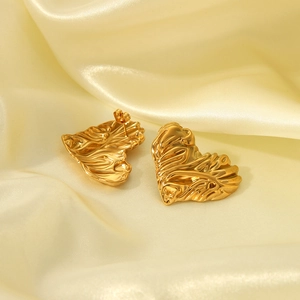 Détail des boucles d'oreilles cœur dorées avec texture lave sur tissu en soie