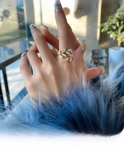 Close-up of a gold leaf ring with opal accents worn against a blue faux fur background