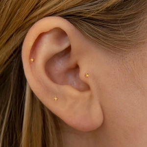 Detailed view of three gold star piercing studs worn on helix, tragus and earlobe
